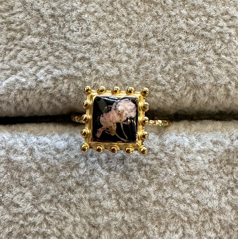 Gold ring with a black and white floral design on a textured beige surface