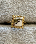 Gold ring with a square design on a textured gray surface