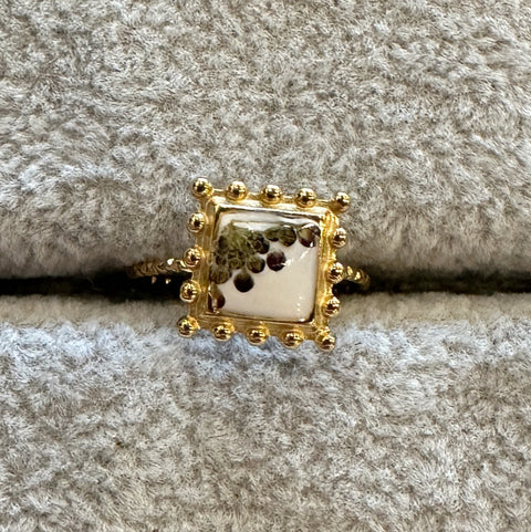 Gold ring with a square design on a textured gray surface