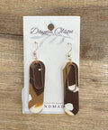 Pair of earrings on a card with 'Dayna Olson' branding on a wooden surface