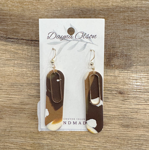 Pair of earrings on a card with 'Dayna Olson' branding on a wooden surface