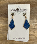 Pair of blue earrings with star accents on a branded card, placed on a wooden surface.