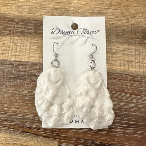 White coral-like earrings on a branded card against a wooden background