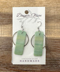 Green earrings on a card with 'Dayna Olson' branding on a wooden surface
