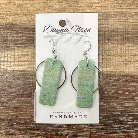 Green earrings on a card with 'Dayna Olson' branding on a wooden surface