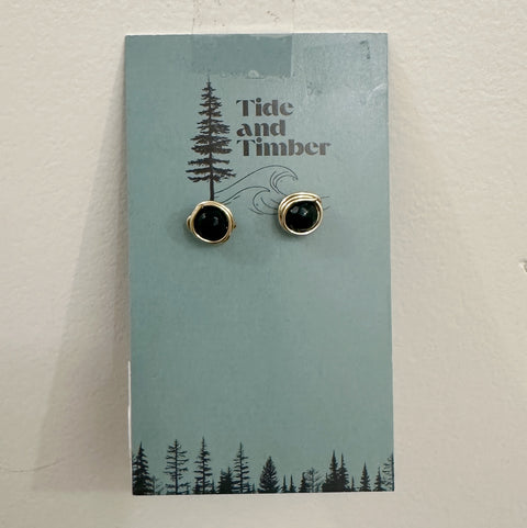 Pair of black stud earrings on a 'Tide and Timber' branded card with a forest design.