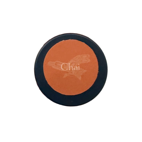 Round makeup product with 'Chai' branding held by a hand against a neutral background