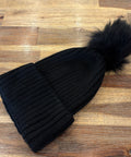 Black knit beanie with a fur pom-pom on a wooden surface