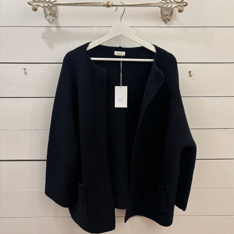 Black cardigan on a hanger against a white wooden panel background