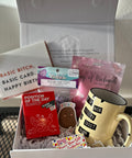 Gift box with a mug, cards, and other items on a metal surface.