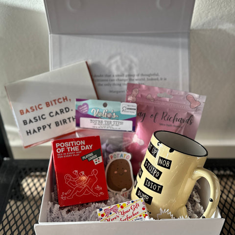 Gift box with a mug, cards, and other items on a metal surface.