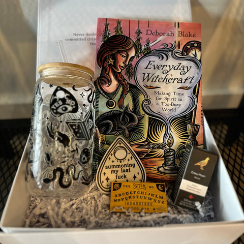 Box containing a glass jar with black designs, a book titled 'Everyday Witchcraft', and other items.
