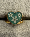Heart-shaped ring with floral design on a textured surface