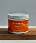 Candle jar labeled 'Raven Song Pumpkin Spice' on a wooden surface with a gray background