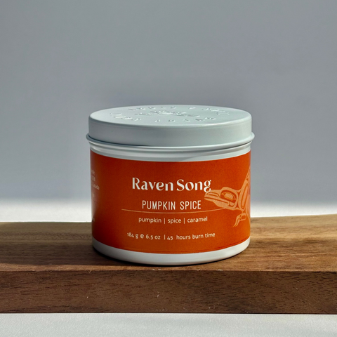 Candle jar labeled 'Raven Song Pumpkin Spice' on a wooden surface with a gray background