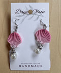 Pink shell earrings with pearl drops on a 'Dayn Olson' card against a wooden background