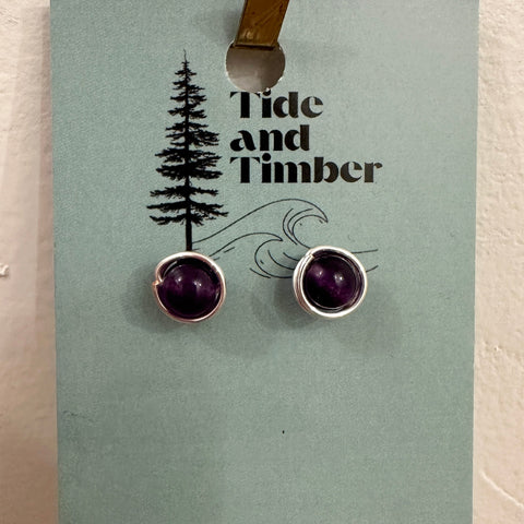 Pair of purple gemstone earrings on a 'Tide and Timber' branded card.