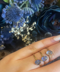 Hand wearing two rings with purple gemstones against a floral background