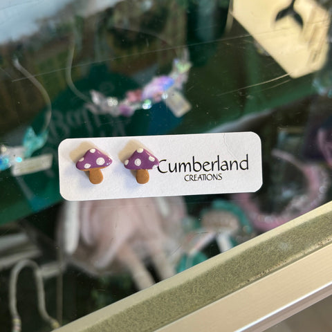 Two mushroom-shaped earrings on a 'Cumberland' branded card, with a blurred background.