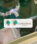Earrings with turquoise and gold designs on a 'Cumberland' label against a blurred background.