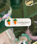 Carrot-shaped earrings on a 'Cumberland' card with a blurred background of jewelry.