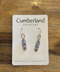 Pair of earrings on a 'Cumberland Creations' card against a wooden background