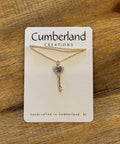 Gold necklace with pendant on a Cumberland Creations card on a wooden surface