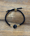 Bracelet with black cord and gold accents on a wooden surface