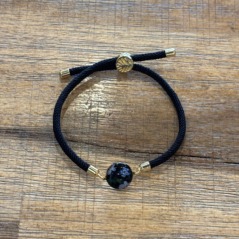 Bracelet with black cord and gold accents on a wooden surface