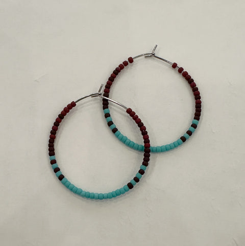 Pair of hoop earrings with turquoise and red beads on a light gray background