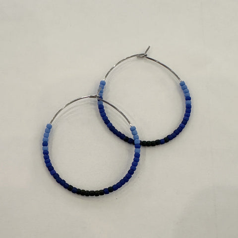 Pair of hoop earrings with blue and black beaded accents on a light gray background