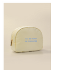 A cream-colored zippered cosmetic bag with light blue text reading 'I'LL BE READY IN 5 MINUTES' on the front, set against a solid beige background.