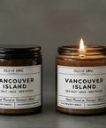 Two amber glass jar candles labeled Vancouver Island by Isle of Rose Candle Co. One jar is closed with a black lid, and the other is open and lit, showing a warm flame against a soft gray background.