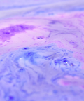 A close-up of a marbled liquid with swirling pastel purple, pink, and blue tones.