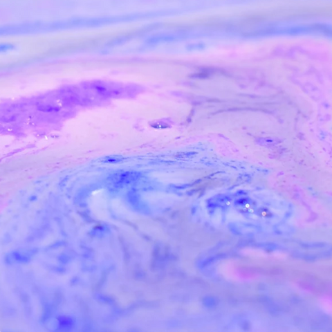 A close-up of a marbled liquid with swirling pastel purple, pink, and blue tones.