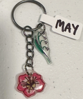 Keychain with floral charm and 'MAY' tag on a light gray background