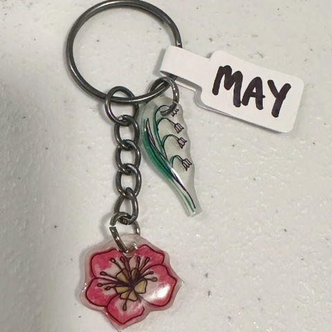 Keychain with floral charm and 'MAY' tag on a light gray background