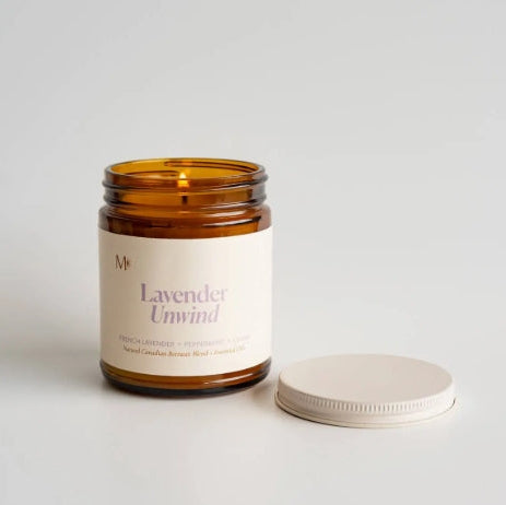 Candle in a glass jar labeled 'Lavender Unwind' on a light background