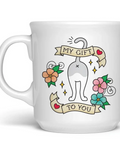 A white ceramic coffee mug featuring a cartoon cat illustration with banners that read 'MY GIFT' and 'TO YOU', surrounded by colorful flowers. The mug is shown on a white background with a Fred.