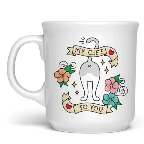 A white ceramic coffee mug featuring a cartoon cat illustration with banners that read 'MY GIFT' and 'TO YOU', surrounded by colorful flowers. The mug is shown on a white background with a Fred.
