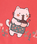 A close-up of a coral pink children's T-shirt with a cute cartoon cat wearing a floral apron and holding a bowl of noodles. The text 'Coton biologique' is visible in the top right corner, indicating organic cotton.