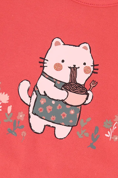 A close-up of a coral pink children's T-shirt with a cute cartoon cat wearing a floral apron and holding a bowl of noodles. The text 'Coton biologique' is visible in the top right corner, indicating organic cotton.