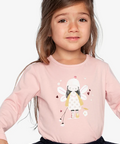 A young girl wearing a light pink long-sleeve t-shirt with a cartoon fairy graphic on the front, paired with a navy blue polka-dot tutu skirt, set against a plain light gray background.