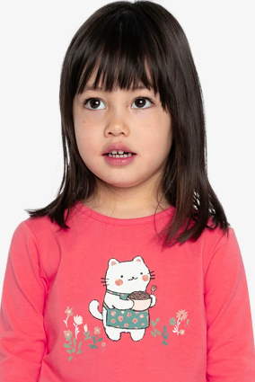 A young girl with dark hair wearing a bright pink long-sleeve shirt with a cartoon cat graphic and pink floral pants, photographed against a light gray background.