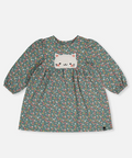A long-sleeve children's dress in a muted sage green fabric with a dense multicolor floral print, featuring a white embroidered cat face patch on the chest.