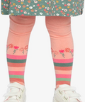A child wearing a green floral dress, pink leggings with a floral and striped pattern, and white sneakers, shown from the waist down against a plain light background.