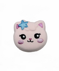 A cute, round, plush cat-face accessory in pale pink with embroidered black eyes, a pink nose, and glittery blue and pink accents on its ears, shown on a plain white background.