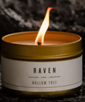 Candle in a tin labeled 'Raven' by Hollow Tree on a dark background