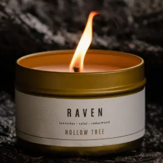 Candle in a tin labeled 'Raven' by Hollow Tree on a dark background