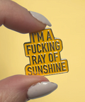 Enamel pin with text held by a hand against a yellow background